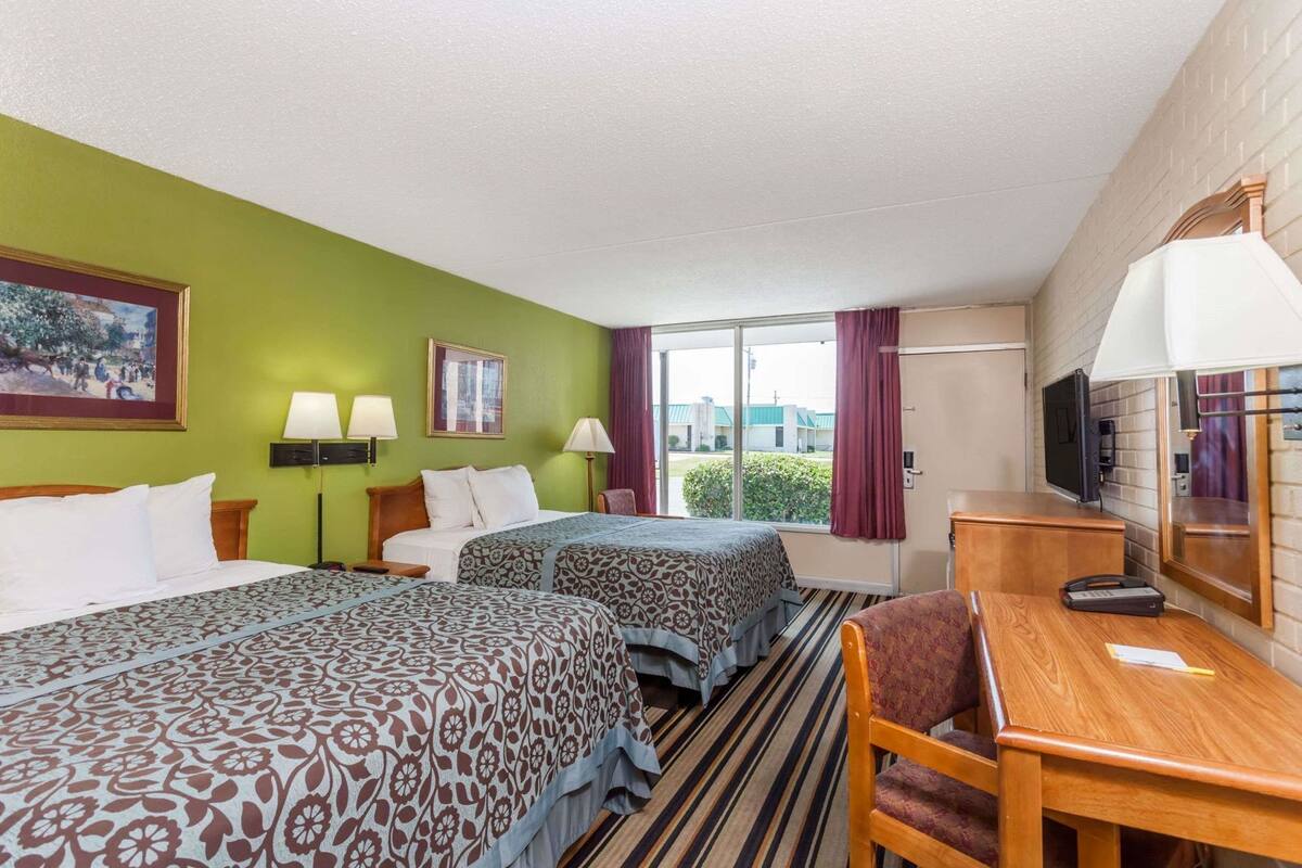 Une chambre d’hôtel avec deux lits, un bureau, une chaise, une télévision et une fenêtre avec des rideaux.