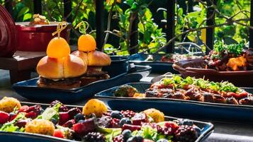 A variety of dishes on a table, including burgers, grilled meats, and a fruit salad.