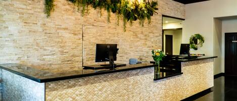 Zona de recepción con pared de ladrillo, mostrador de recepción, monitor de computadora y una planta.