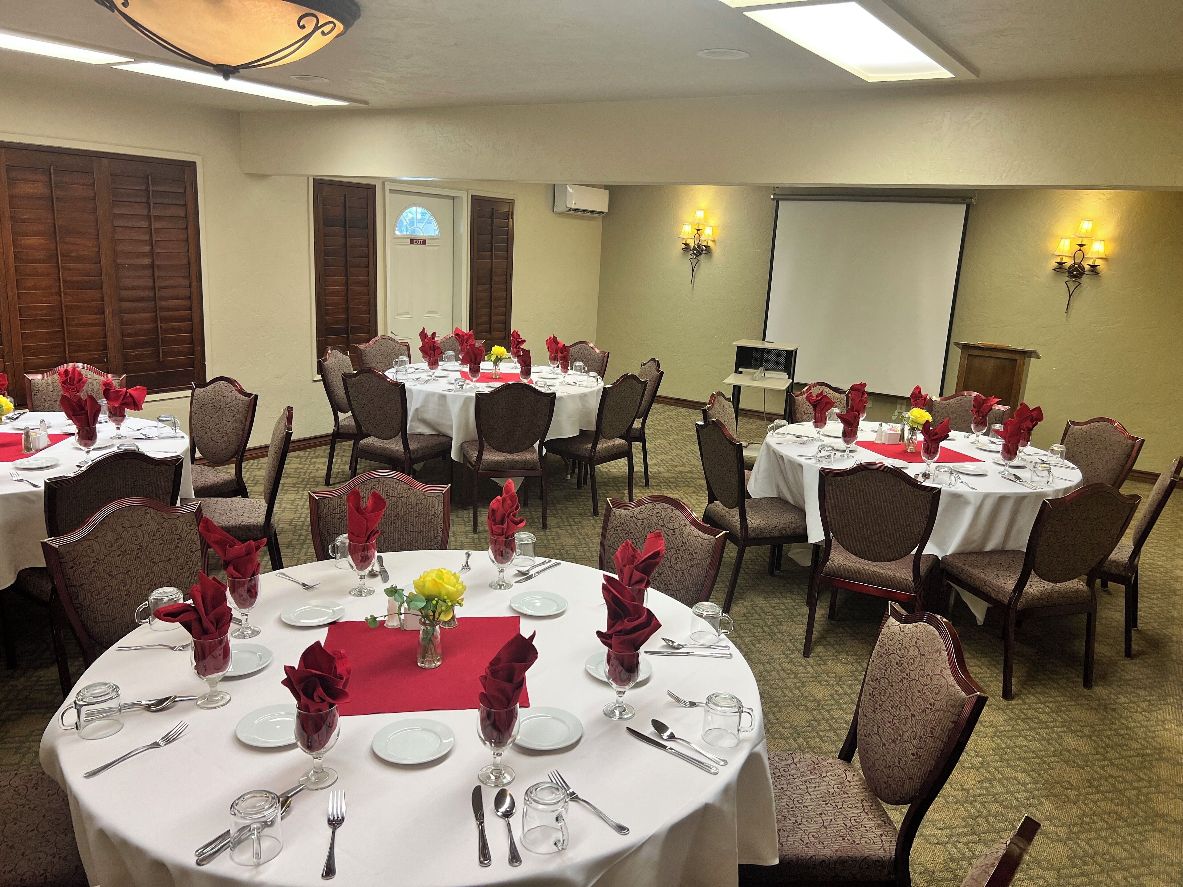 A conference room with multiple round tables, each set with white tablecloths, red napkins, and glassware.