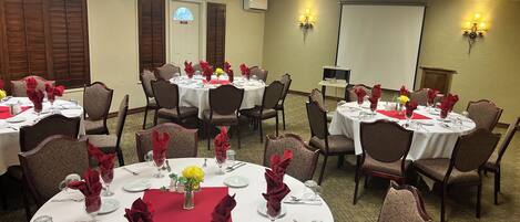 A conference room with multiple round tables, each set with white tablecloths, red napkins, and glassware.