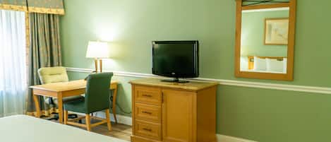 A hotel room with a bed, a desk with a chair, a television on a wooden cabinet, and a mirror on the wall.