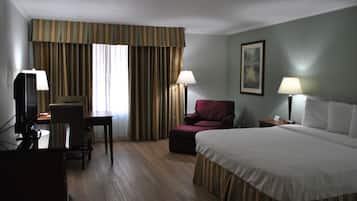 A hotel room with a bed, a desk with a chair, a television, and a lamp.