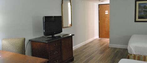 Habitación de hotel con tocador de madera, televisor, cama y puerta que da a otra habitación.