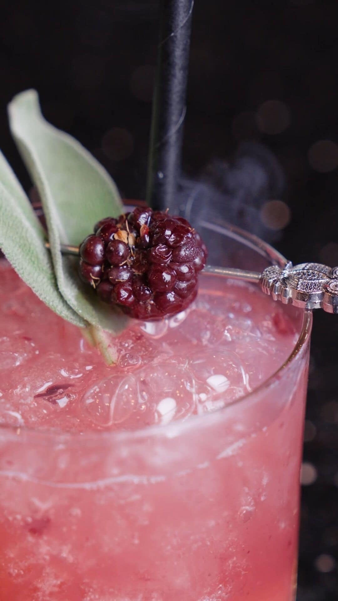 A glass of red beverage with a blackberry garnish and a decorative metal piece.