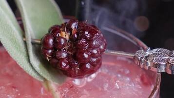 A glass of red beverage with a blackberry garnish and a decorative metal piece.
