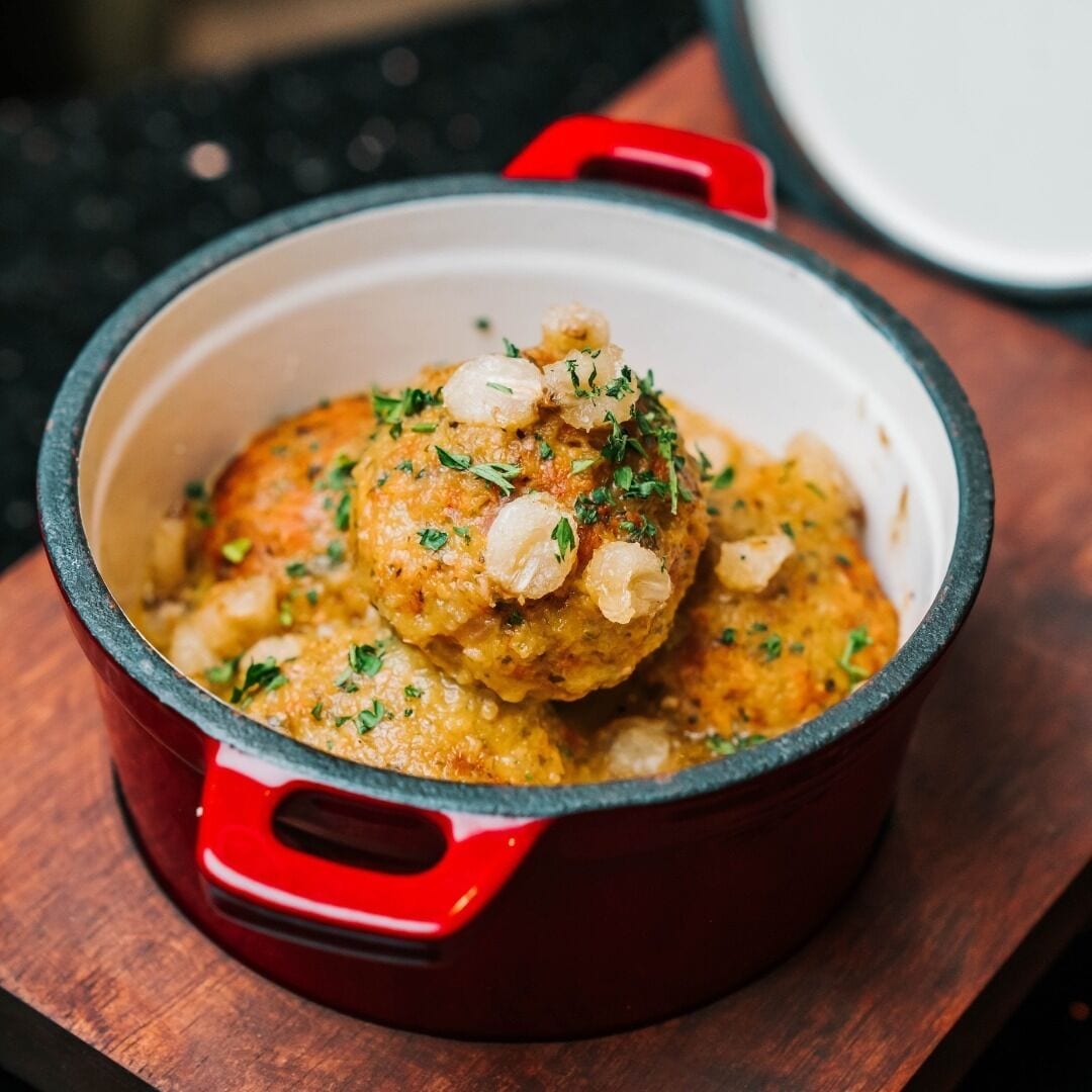 A red pot with a lid, containing a dish garnished with herbs, placed on a wooden surface.