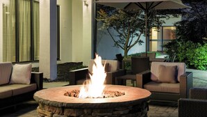 An outdoor seating area with a stone fire pit, wicker furniture, and an umbrella. - Courtyard by Marriott Cincinnati Blue Ash (Cincinnati)