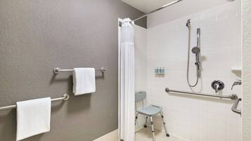 A bathroom with a shower, grab bars, a wheelchair-accessible bench, and a towel rack.