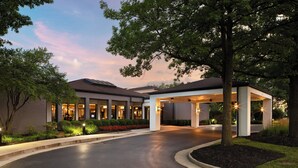 A modern hotel entrance with a covered driveway, landscaped gardens, and illuminated exterior lighting. - Courtyard by Marriott Cincinnati Blue Ash (Cincinnati)