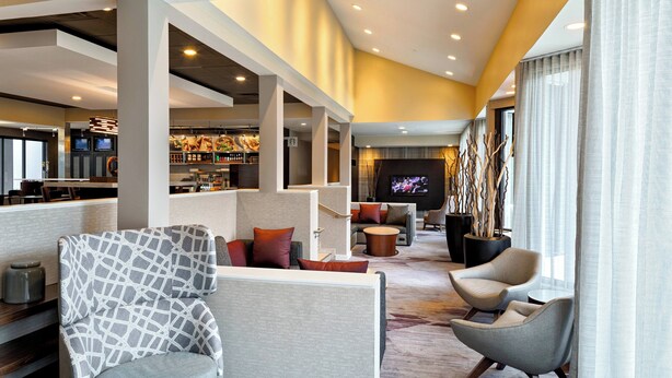 A modern hotel lobby with seating areas, a bar, and a television screen. - Courtyard by Marriott Cincinnati Blue Ash (Cincinnati)