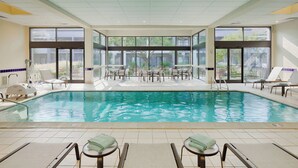 An indoor swimming pool with clear glass walls, lounge chairs, and tables. - Courtyard by Marriott Cincinnati Blue Ash (Cincinnati)