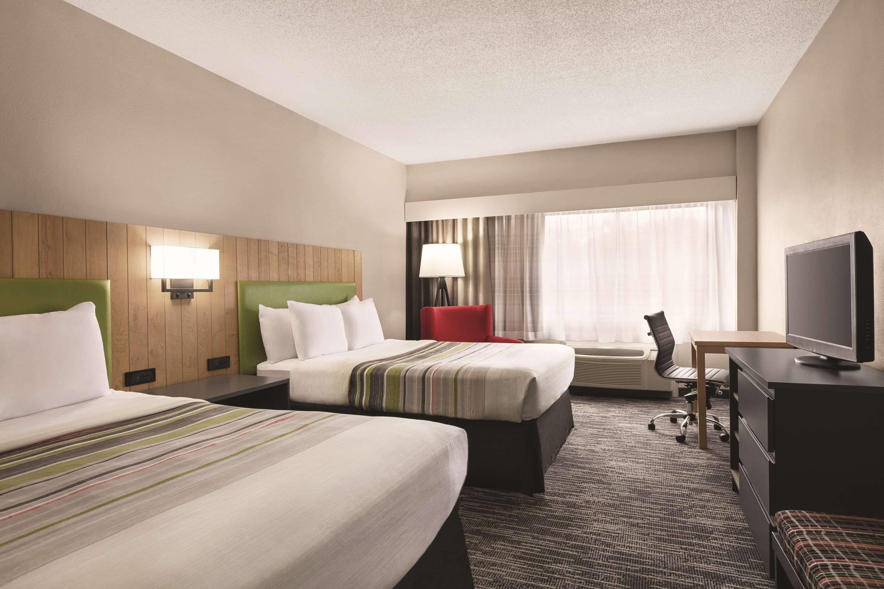 A hotel room with two beds, a desk, a chair, a television, and a window with curtains.