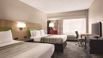 A hotel room with two beds, a desk, a chair, a television, and a window with curtains.
