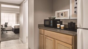 A modern hotel room with a kitchenette, a bed, a desk, and a view of the city. - Country Inn & Suites by Radisson, Williamsburg East (Busch Gardens), VA (Williamsburg)