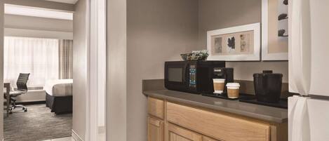 A modern hotel room with a kitchenette, a bed, a desk, and a view of the city.