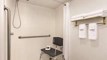 Un baño con ducha, barras de apoyo, un asiento accesible para silla de ruedas y un perchero para toallas.