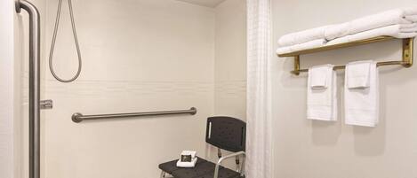 Un baño con ducha, barras de apoyo, un asiento accesible para silla de ruedas y un perchero para toallas.
