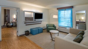 A modern hotel room with a flat-screen TV, a green armchair, a beige sofa, and a small round table. - EVEN Hotel Norwalk by IHG (Norwalk)