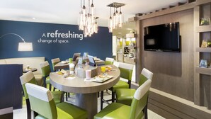 A modern dining area with a round table, green chairs, a flat-screen TV, and a wall with a text message. - EVEN Hotel Norwalk by IHG (Norwalk)