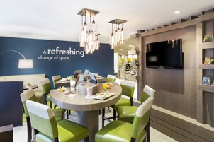 A modern dining area with a round table, green chairs, a flat-screen TV, and a wall with a text message.