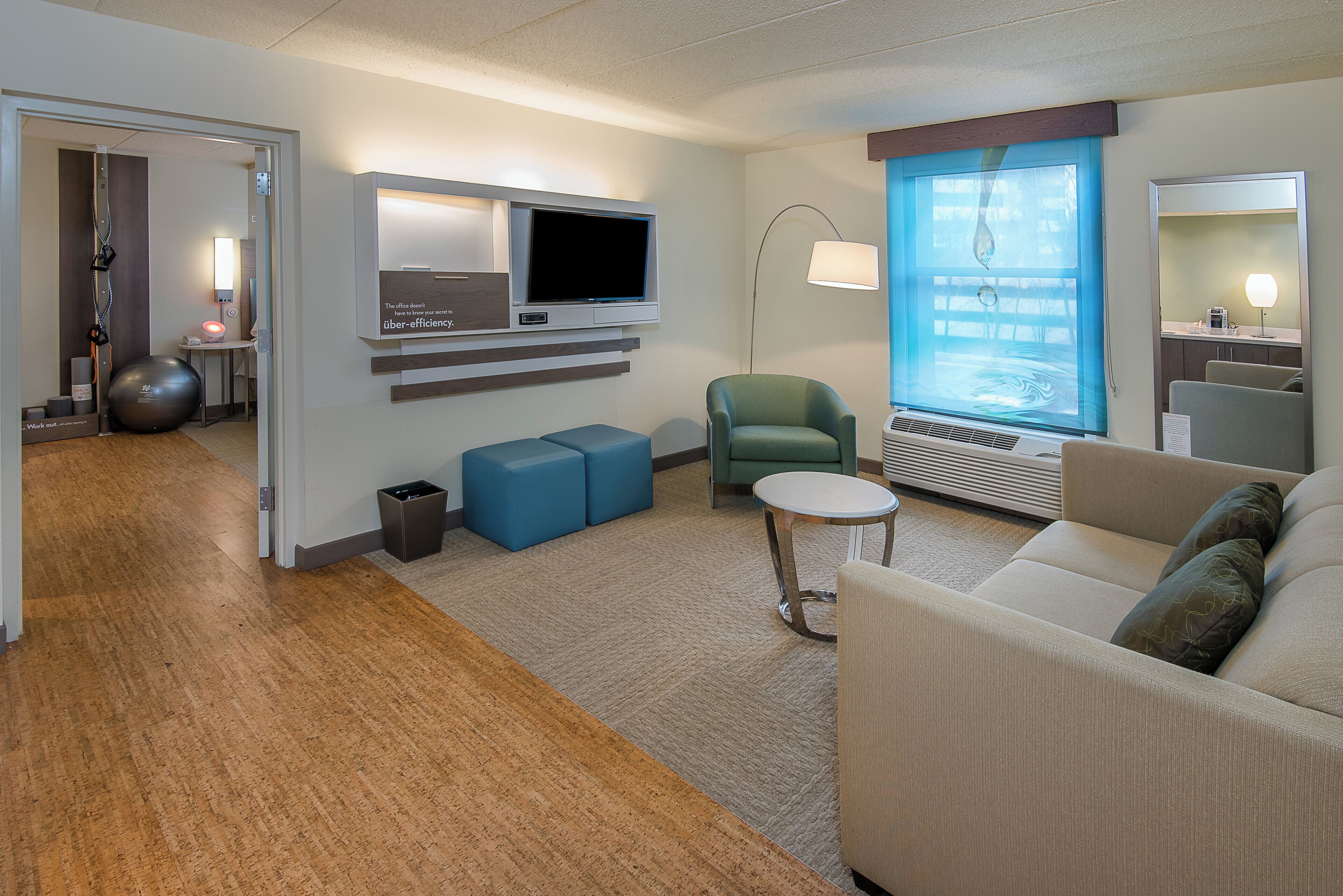 Habitació d'hotel moderna amb televisió de pantalla plana, una butaca verda, una taula rodona petita i un sofà amb mirall.