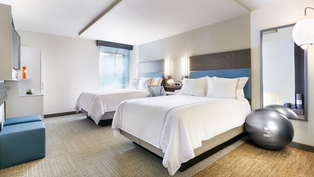A hotel room with two beds, a large mirror, exercise ball, and a window with blinds. - EVEN Hotel Norwalk by IHG (Norwalk)