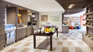 A modern kitchen area with a central table displaying fruits and condiments, a built-in oven, and a counter with bottled water. - EVEN Hotel Norwalk by IHG (Norwalk)