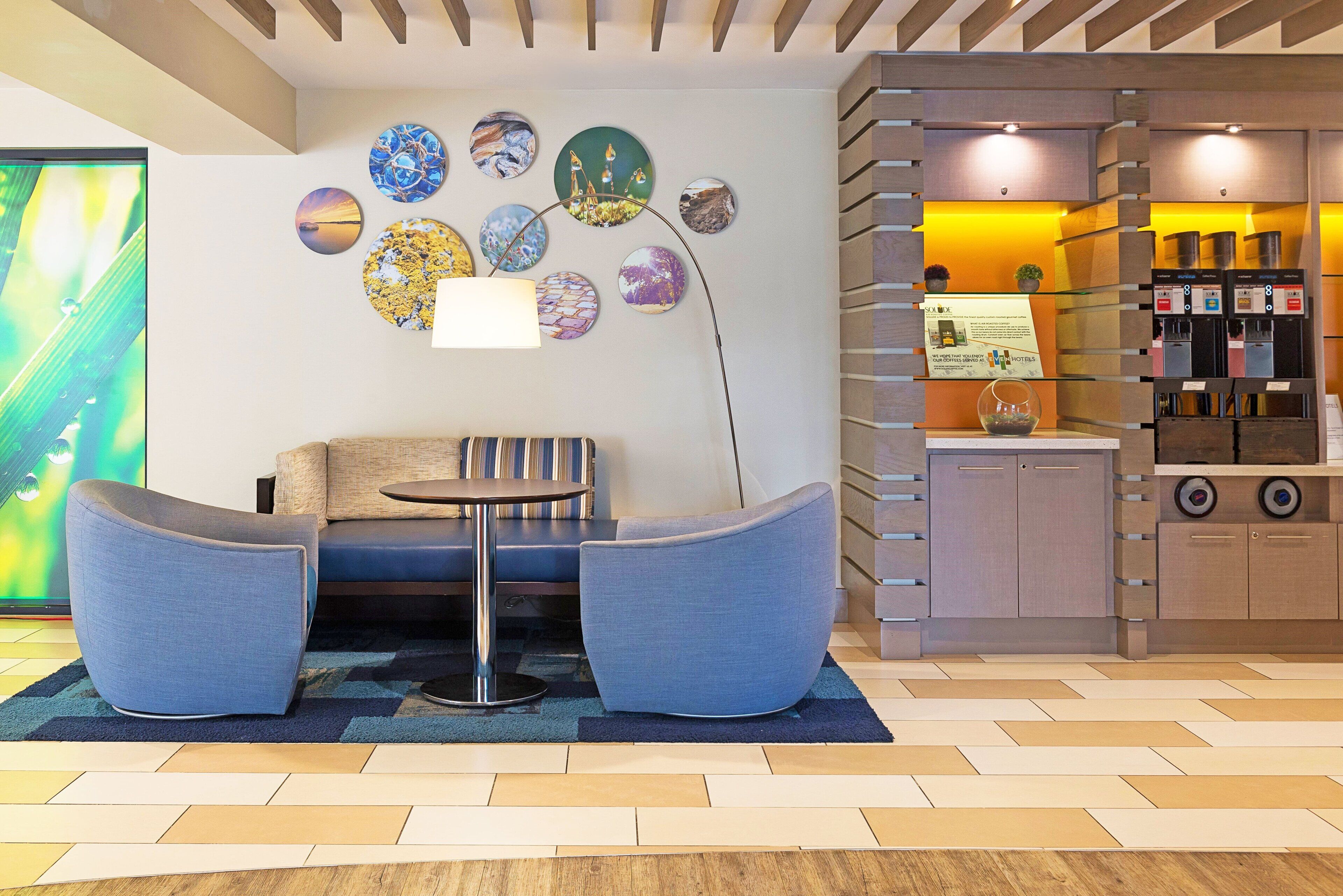 A modern hotel lobby with a seating area, a coffee bar, and a wall decorated with circular art pieces.