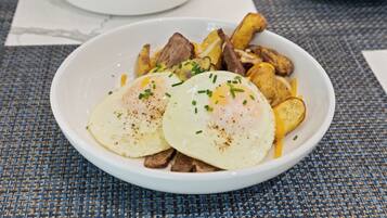 Un bol blanc contenant des œufs, des pommes de terre et de la viande, posé sur une nappe à motifs tissés.
