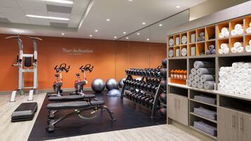 Un gimnasio con equipo de ejercicio, una pared con texto motivacional y toallas y artículos de aseo ordenados.