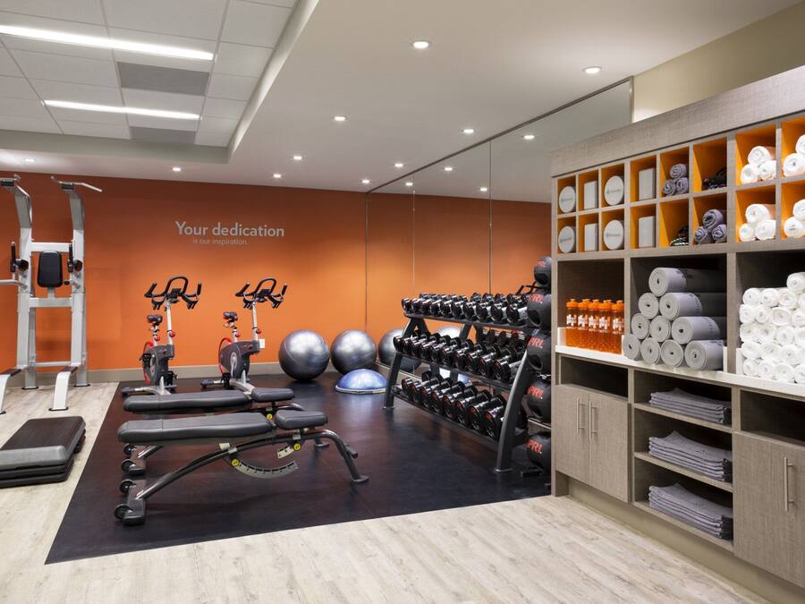 Un gimnasio con equipo de ejercicio, una pared con texto motivacional y toallas y artículos de aseo ordenados.