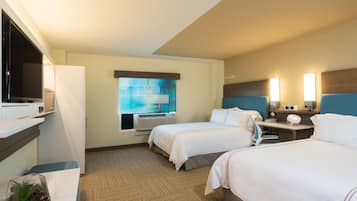 A hotel room with two beds, a flat-screen TV, a desk with a lamp, and a window with a view.