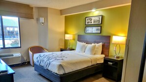 Ein Hotelzimmer mit einem großen Bett, zwei Nachttischen mit Lampen, einem Sessel und einem Fenster mit Klimaanlage.