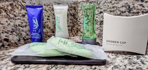 A bathroom counter with a shower cap, a blue lotion tube, a green bottle, and two green soap bars.