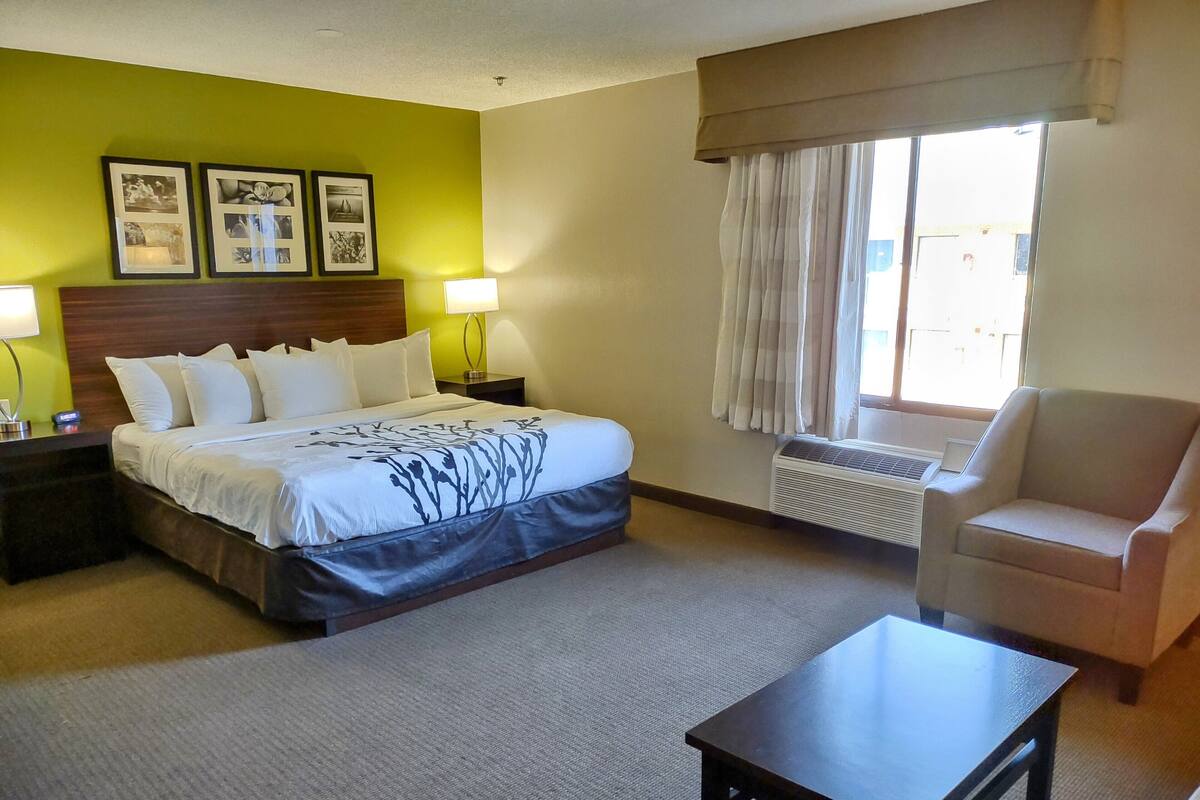 Una habitación de hotel con cama, una silla, una mesa y una ventana con cortinas.