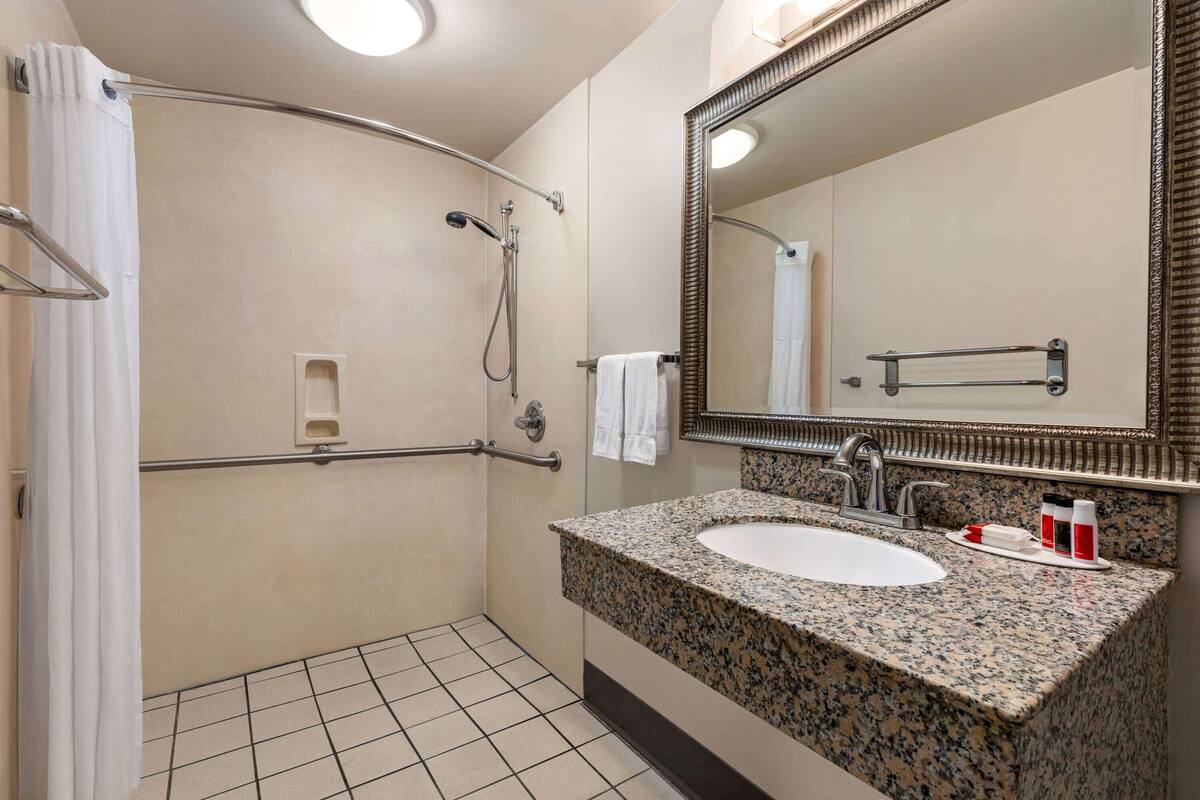 A bathroom with a shower, grab bar, sink, and mirror.