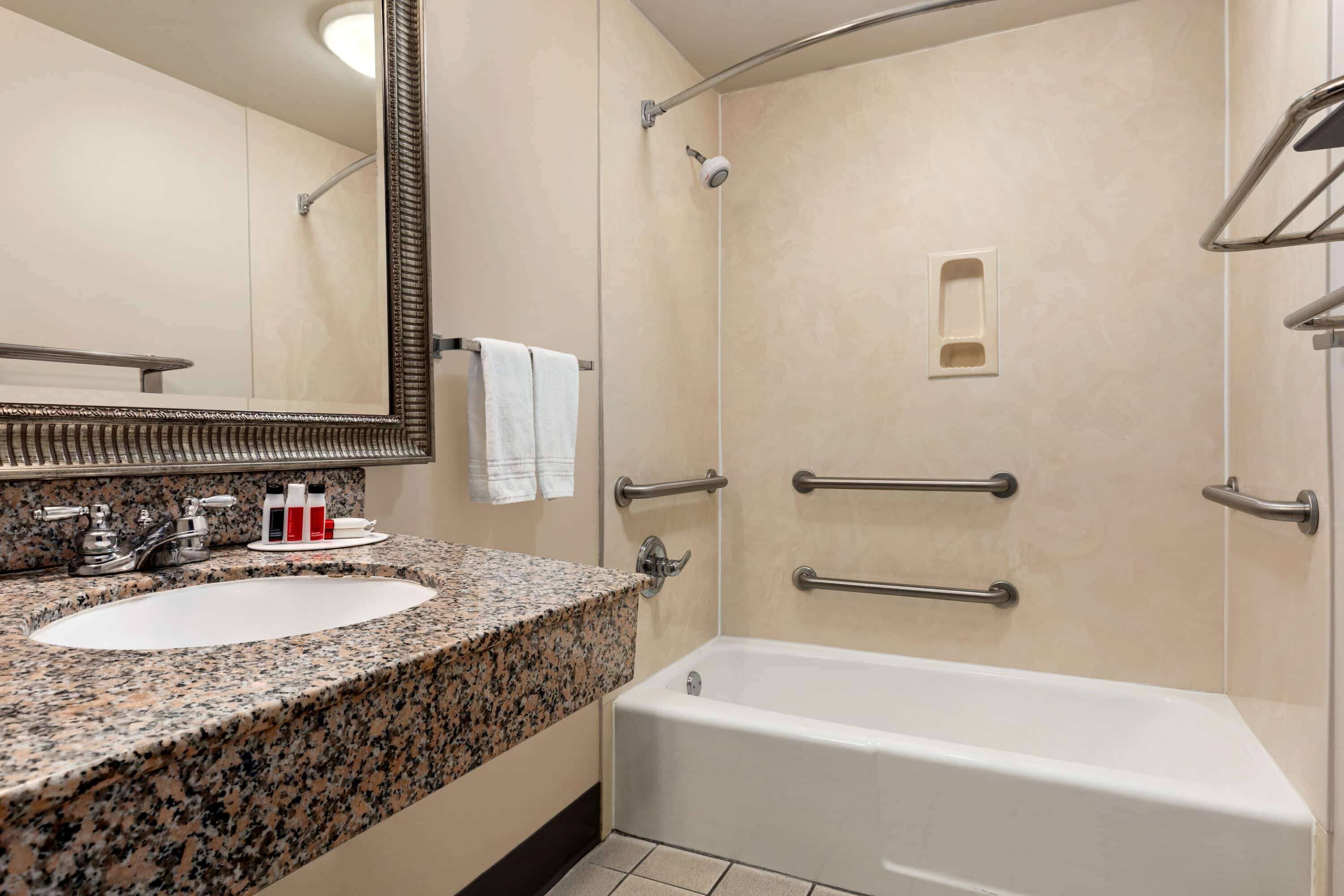 Baño con lavamanos de encimera de granito, bañera blanca y ducha con cabezal de ducha manual.