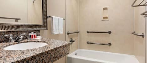 A bathroom with a granite countertop sink, a white bathtub, and a shower with a handheld showerhead.