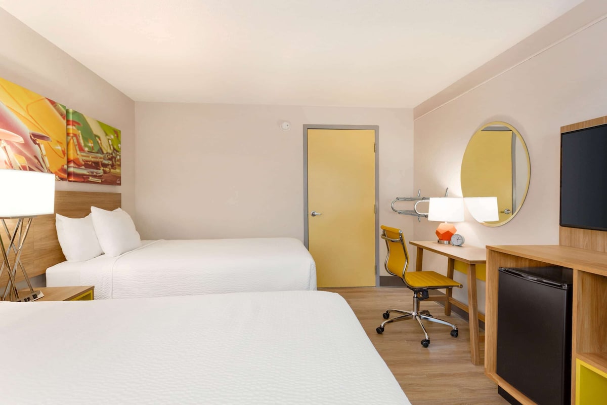 A hotel room with two beds, a desk with a lamp, a chair, a TV, and a door.