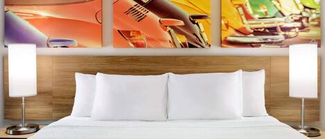 A hotel room with a wooden headboard, white bedding, and three wall-mounted paintings depicting various objects.