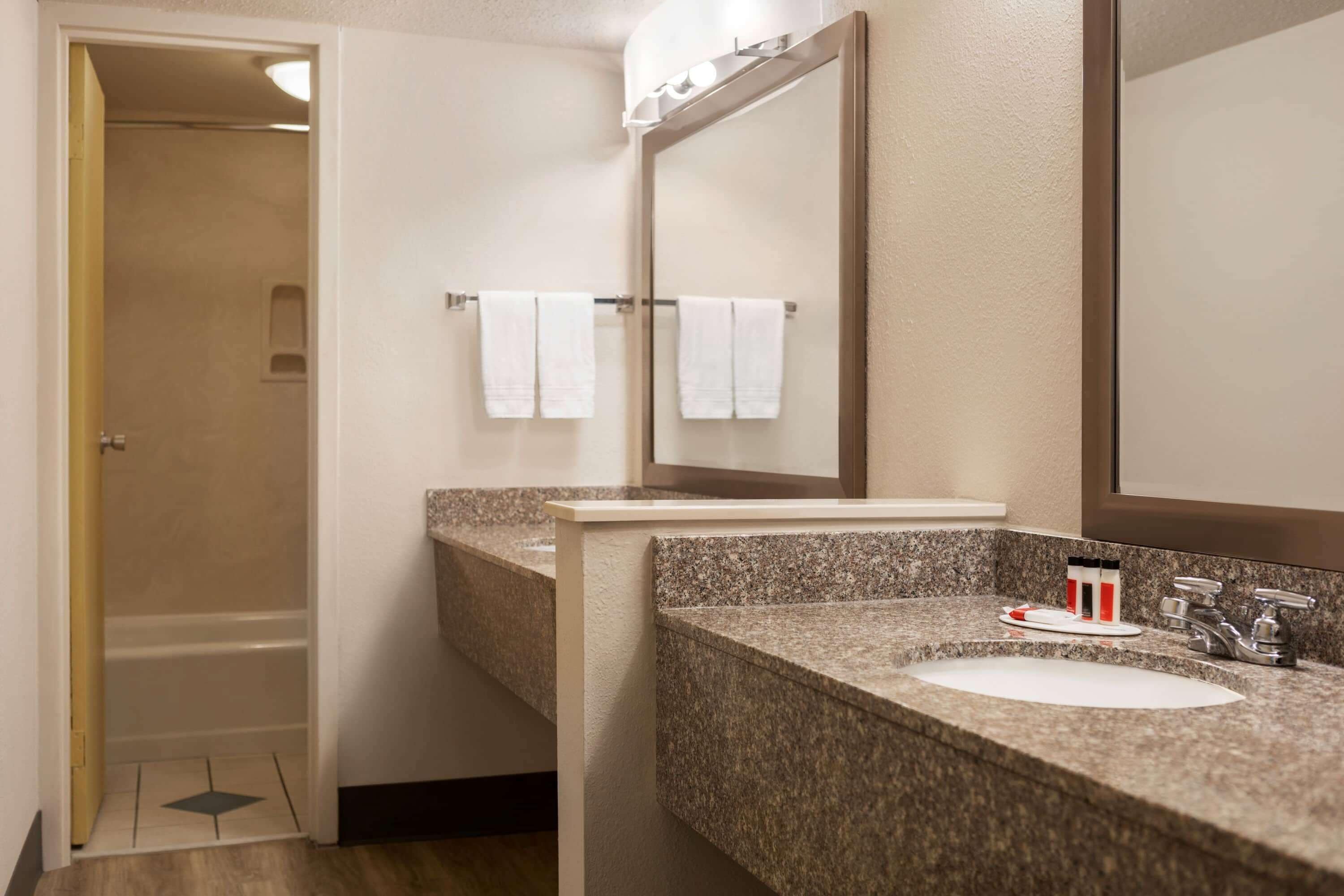 A bathroom with a granite countertop sink, a mirror, and a towel rack with two white towels.