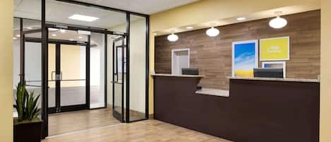 A reception area with a wooden wall, a glass door entrance, and a potted plant.