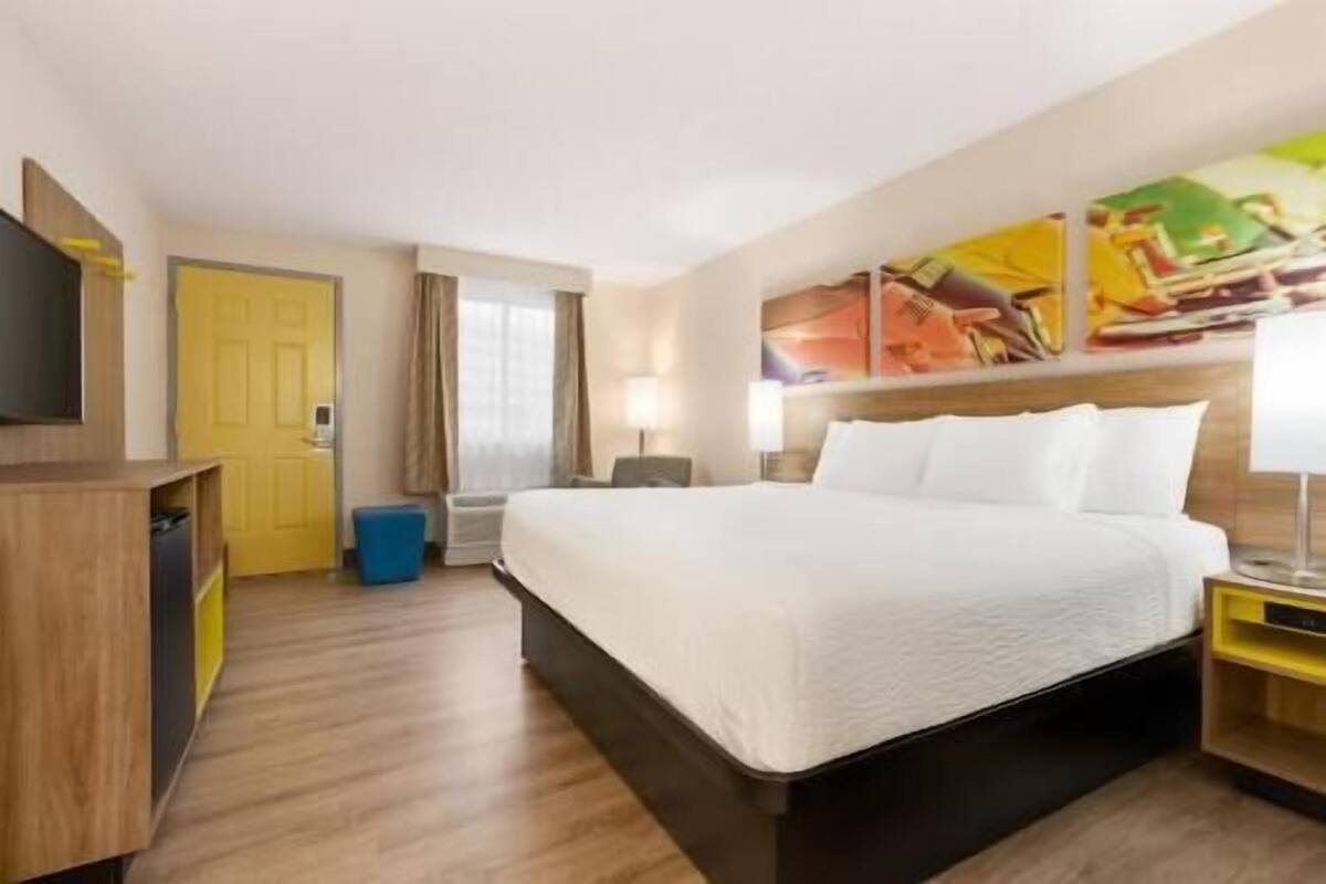 A hotel room with a bed, bedside tables, a desk, a chair, a wardrobe, and a painting on the wall.