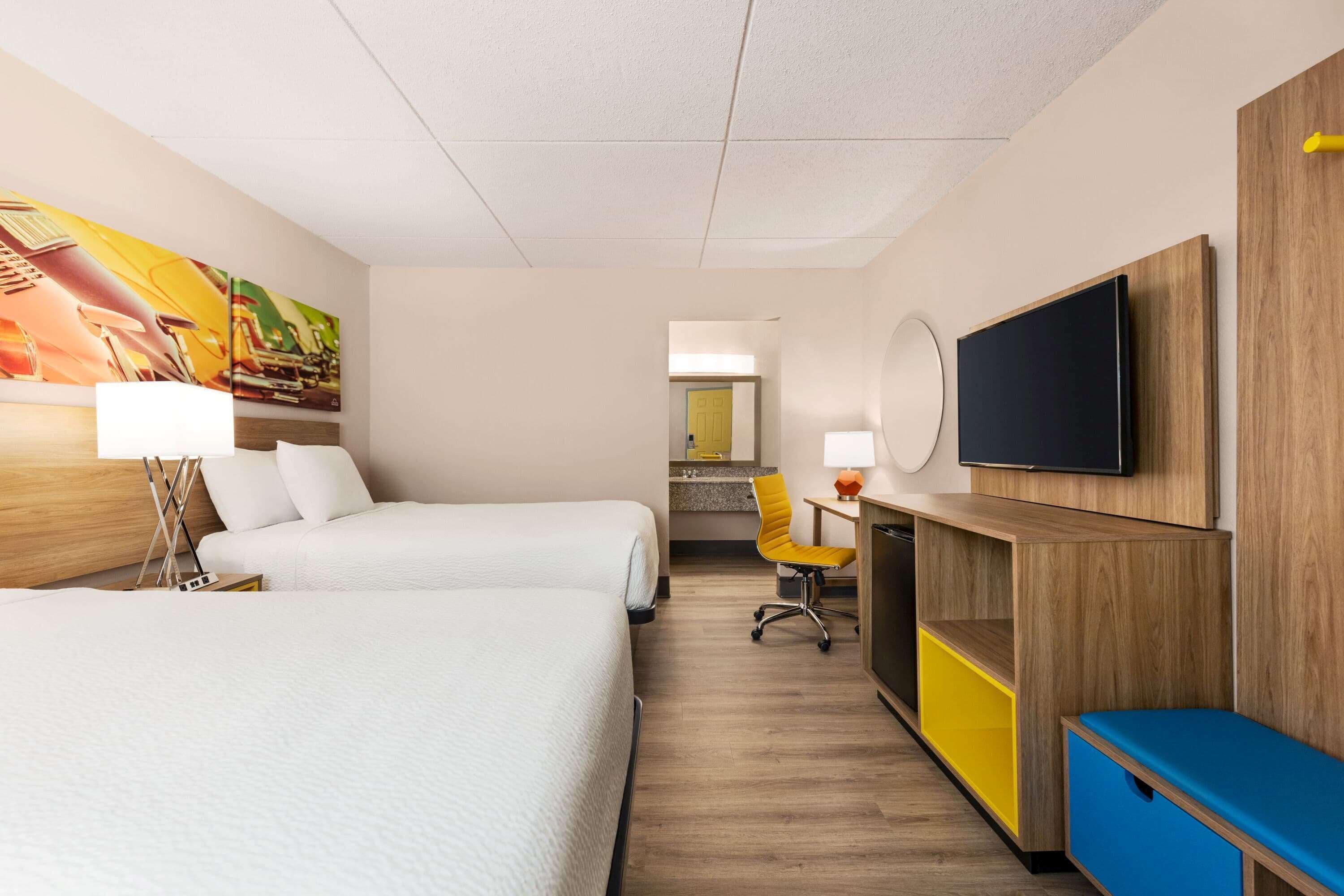 Een hotelkamer met twee bedden, een bureau, een stoel, een televisie en een schilderij aan de muur.