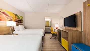 Ein Hotelzimmer mit zwei Betten, einem Schreibtisch, einem Stuhl, einem Fernseher und einem Bild an der Wand.