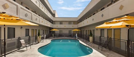 A swimming pool with lounge chairs and umbrellas, surrounded by a building with balconies and windows.
