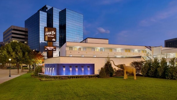 Ein Hotel mit einem modernen Glasgebäude und einem traditionellen Gebäude, ein Brunnen sowie eine Elefantenskulptur.