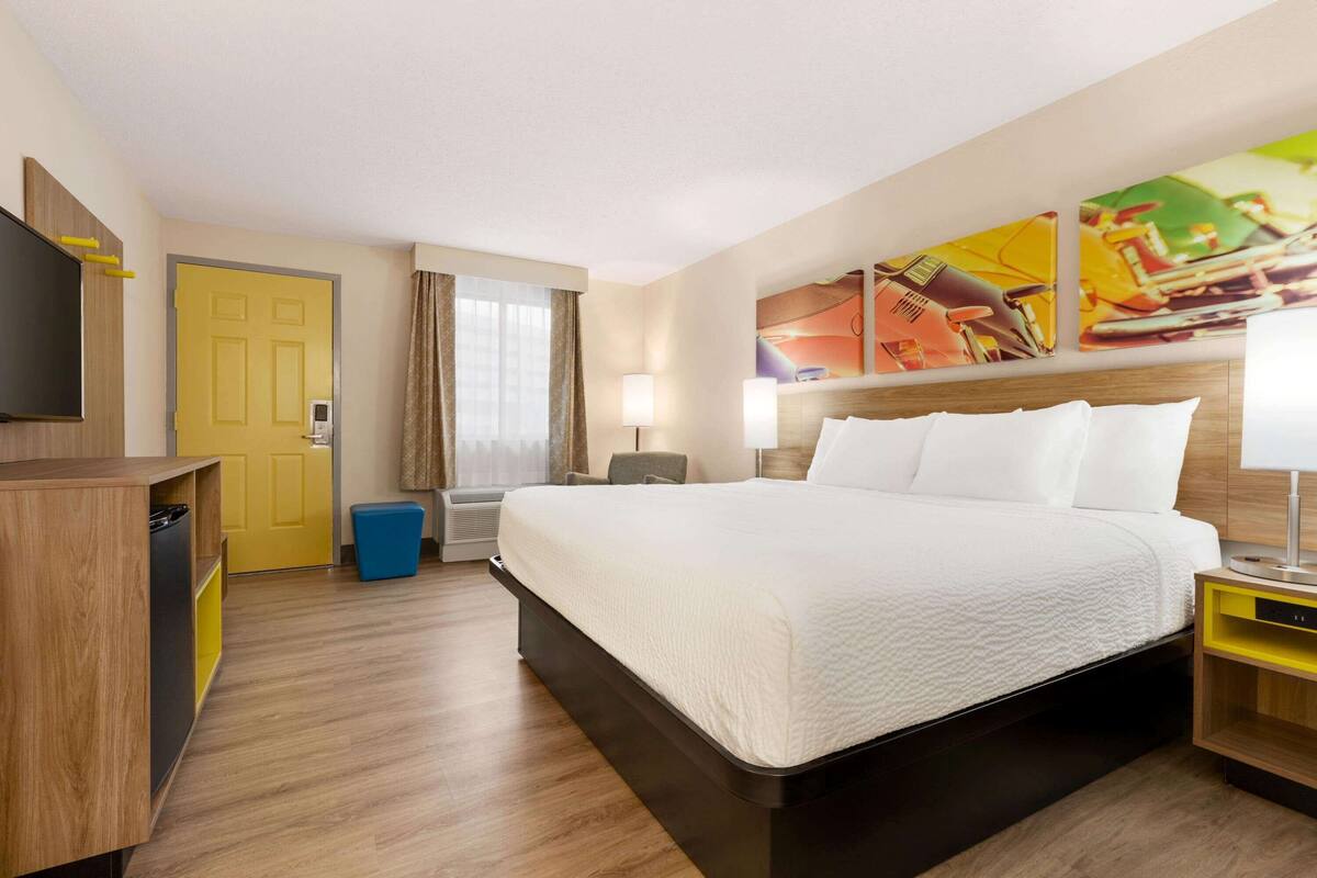 A hotel room with a large bed, a TV, a desk, and a painting on the wall.