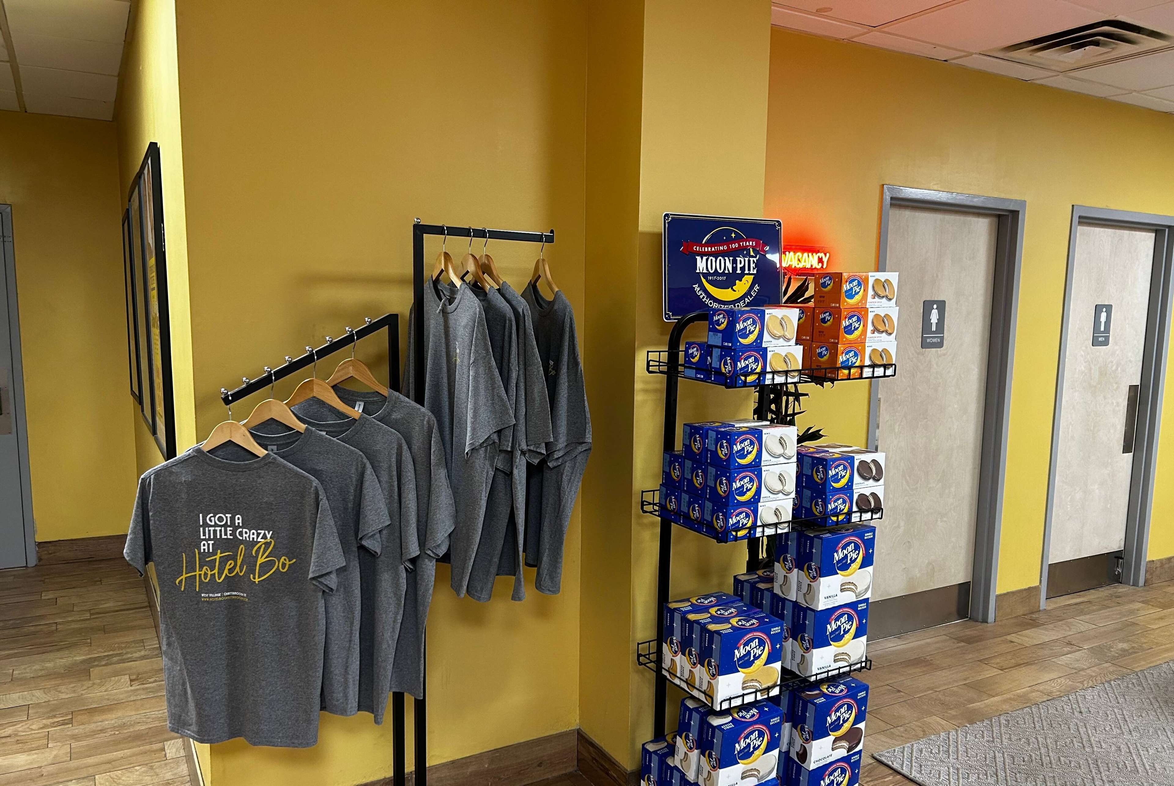 A hotel lobby with a yellow wall, a rack of grey t-shirts, and a display of MoonPie boxes.